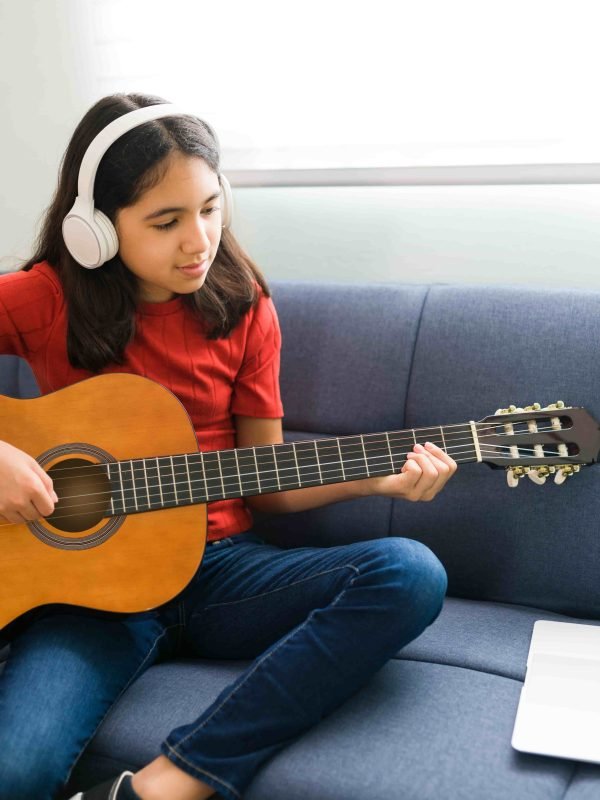 latin-girl-with-headphones-listening-her-online-music-lessons-artistic-kid-playing-acoustic-guitar-learning-chords (1)